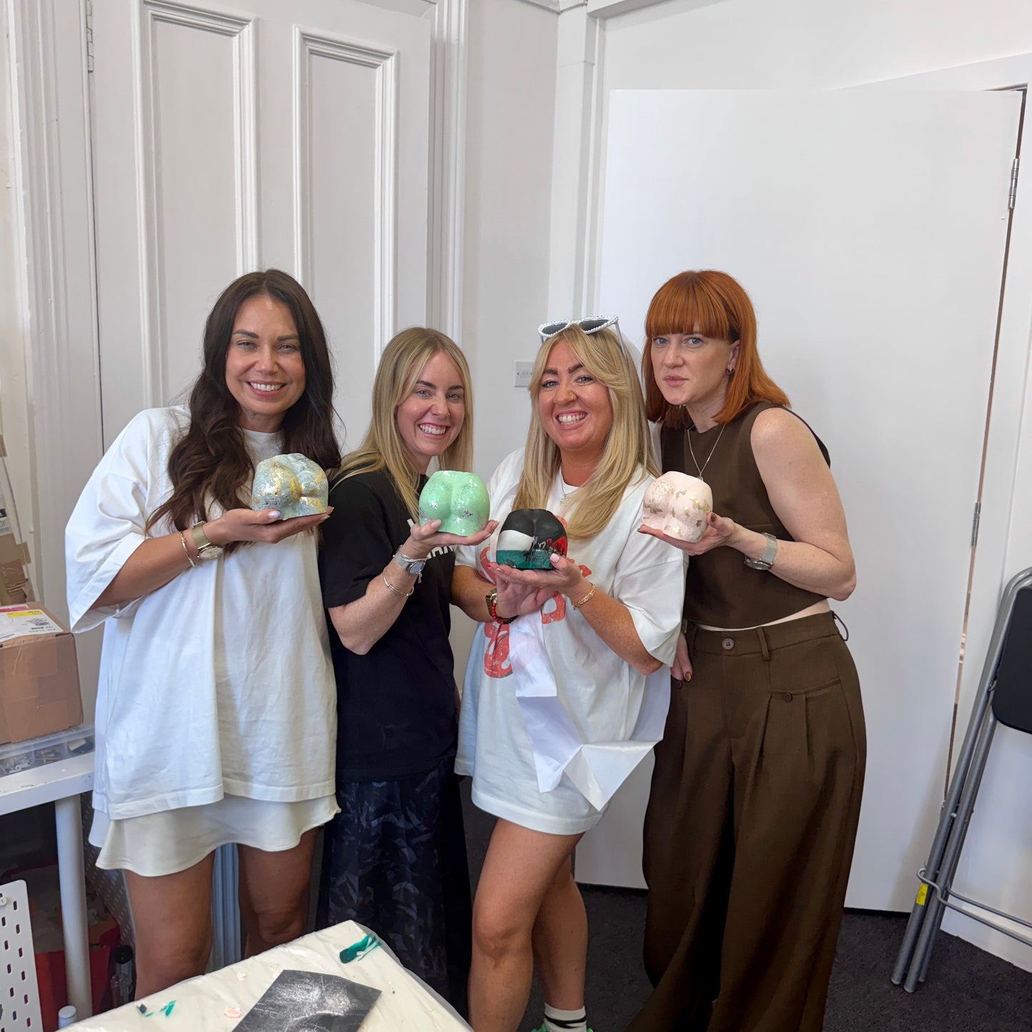 Four women holding Bum Pot made from Jesmonite in a room with white walls and a table.
